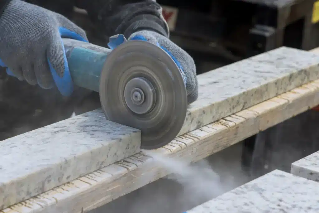Découpe de Granit à la Meuleuse d'Angle : Guide Pratique Artisan découpant une plaque de granit avec une meuleuse d'angle électrique, dégageant de la poussière de pierre.