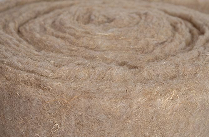 Isolation naturelle : Rouleau de fibres beiges feutrées Rouleau de matériau isolant en fibres naturelles beiges denses, montrant la texture feutrée et le motif en spirale du feutre. Matériau écologique.