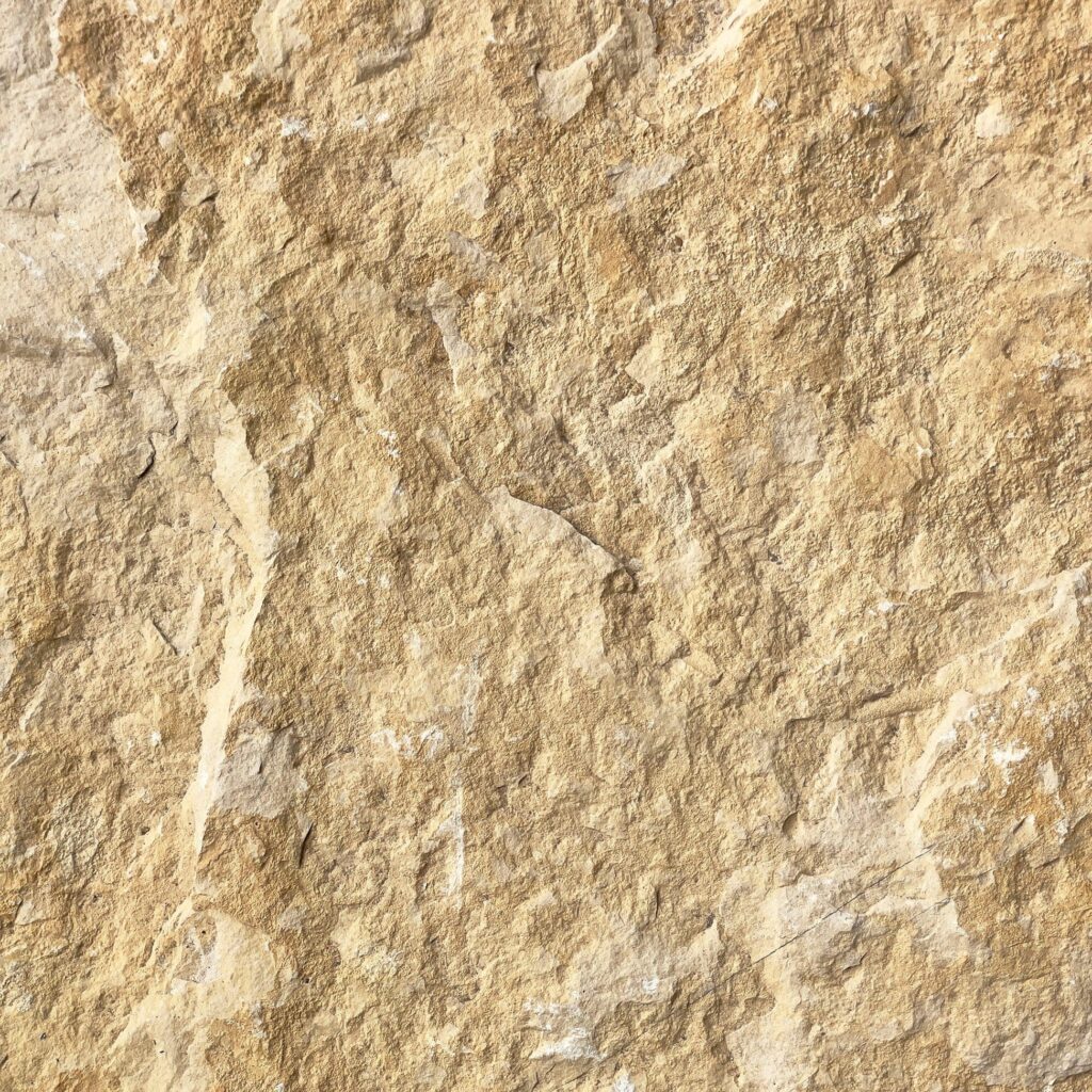 Texture Grès naturel beige : Fond pierre brute et rugueuse. Texture rugueuse et détaillée de pierre naturelle beige ocre. Surface de grès fracturée, reliefs minéraux et fissures profondes.