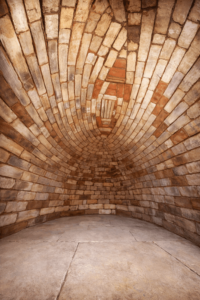 Coupole historique : voûte en briques rustiques et niche Voûte en briques rustiques rouges et beiges formant une coupole. Niche centrale marquée par un motif en arche et une petite grille. Sol en dalles.